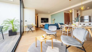 A modern living room with a dining area, a kitchen, and a large sliding glass door leading to a balcony.