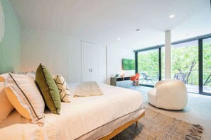 Un dormitorio moderno con una cama grande, un escritorio y vistas a la vegetación a través de amplias ventanas.