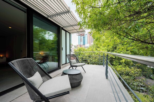 Un área de estar moderna al aire libre con puerta de vidrio que da a una habitación, rodeada de vegetación y vista de la ciudad.