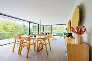 Un comedor moderno con una mesa grande y sillas, un aparador de madera y un amplio ventanal con vistas al verdor.