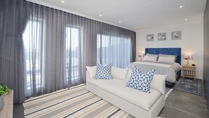 A modern bedroom with a large bed, a sofa, and a nightstand. - HoneyBee Cottage (Yzerfontein)
