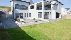 A modern two-story house with large windows, a flat roof, and a well-maintained lawn. - HoneyBee Cottage (Yzerfontein)