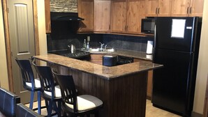 A kitchen with wooden cabinets, a black refrigerator, a built-in island with bar stools, and a stone accent wall.