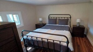 A bedroom with a metal bed frame, a wooden dresser, two bedside tables with lamps, and a window with blinds.