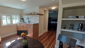 A kitchen with a stainless steel refrigerator, a wooden dining table with a vase, and a window with blinds.
