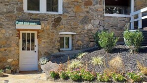 A stone house with a white door, a small window, and a stone pathway leading to the entrance.