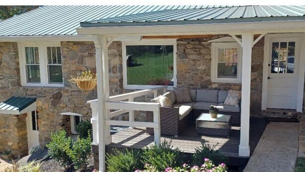 A stone house with a covered porch, outdoor seating, and a stone fireplace.