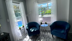 Una habitación con dos sillones azules, una mesita redonda y una ventana con cortinas blancas.