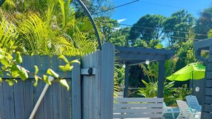 Una verja de madera con un murciélago colgando, que da acceso a un patio con una pérgola y mobiliario exterior.