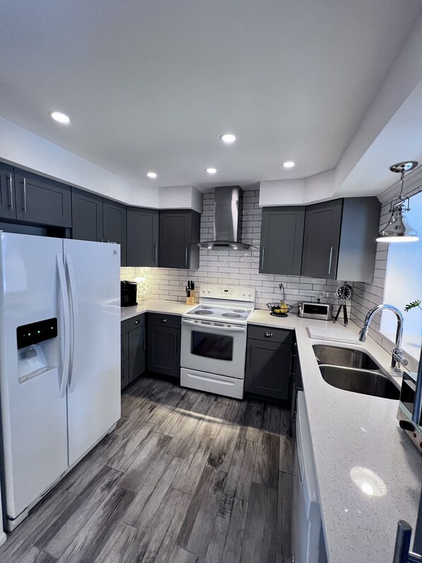 A modern kitchen with dark cabinets, a white refrigerator, a stove, and a sink. - New Luxurious Coastal Resort 3-Beedroom 2 Bath Private Pool
(Venice)
