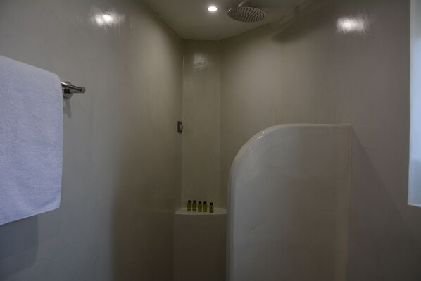 A bathroom with a shower, a towel rack, and a shelf with toiletries.