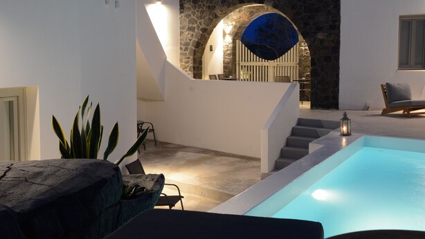 A modern outdoor pool area with a stone wall, a staircase, and a seating area. - Noir Santorini (Santorini)