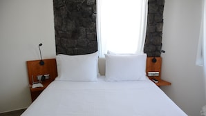 A neatly made bed with white linens, a wooden headboard, and a stone accent wall. - Noir Santorini (Santorini)