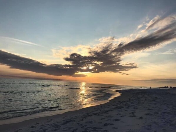 Una playa con atardecer, agua tranquila y cielo despejado.