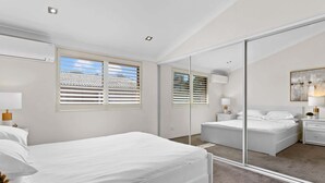 A modern bedroom with a large mirror, a bed, a nightstand, and a window with blinds.
