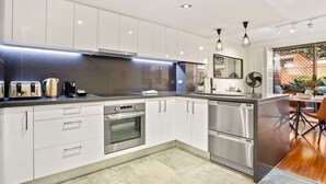 A modern kitchen with stainless steel appliances, white cabinetry, and a dining area with a wooden table and chairs.