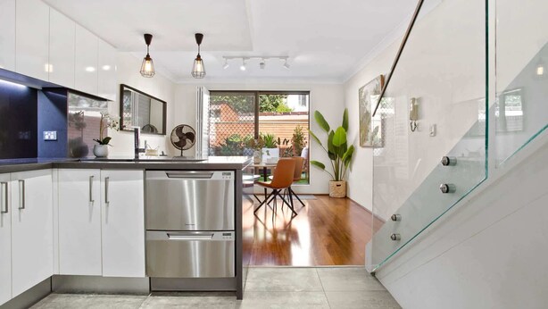A modern kitchen with stainless steel appliances, a dining area with a glass table, and a view of the outdoors.
