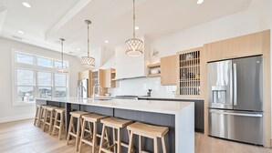 A modern kitchen with a large island, wooden stools, stainless steel appliances, and pendant lighting. - BEACHFRONT Multi-Family Home, 3 levels with decks! (Brigantine)