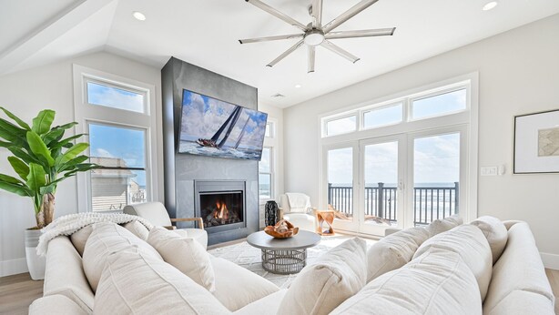A spacious living room with a fireplace, a large flat-screen TV, and a balcony with a view of the ocean. - BEACHFRONT Multi-Family Home, 3 levels with decks! (Brigantine)
