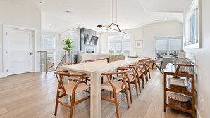 A spacious dining area with a long wooden table and matching chairs, a modern pendant light, and a view of the balcony. - BEACHFRONT Multi-Family Home, 3 levels with decks! (Brigantine)
