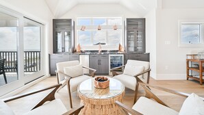 A spacious living area with a large window overlooking a balcony, a kitchen with modern cabinetry, and a round dining table with chairs. - BEACHFRONT Multi-Family Home, 3 levels with decks! (Brigantine)