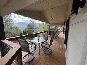 A covered outdoor deck with a table and chairs, a ceiling fan, and a view of mountains and trees. - Saddleback Retreat-Views + Firepit (Sky Valley)