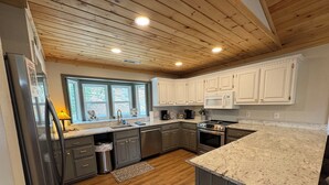 Una cocina moderna con vigas de madera en el techo, armarios blancos, un refrigerador de acero inoxidable y una encimera de granito.