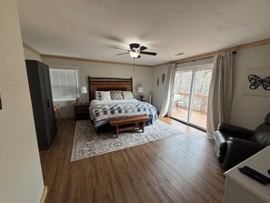A bedroom with a bed, a ceiling fan, a window with blinds, a sliding glass door to a balcony, and a chair. - Saddleback Retreat-Views + Firepit (Sky Valley)