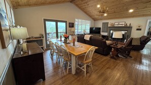 Amplia sala de estar con techo de madera, una mesa de comedor con sillas, chimenea, televisor y sofá.