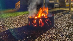 A fire pit with decorative animals, a building with multiple windows, and a patio area with outdoor furniture. - Large, 4 BR (1 King, 2 Queens), 2 Bath, Recently Renovated (Weedville)