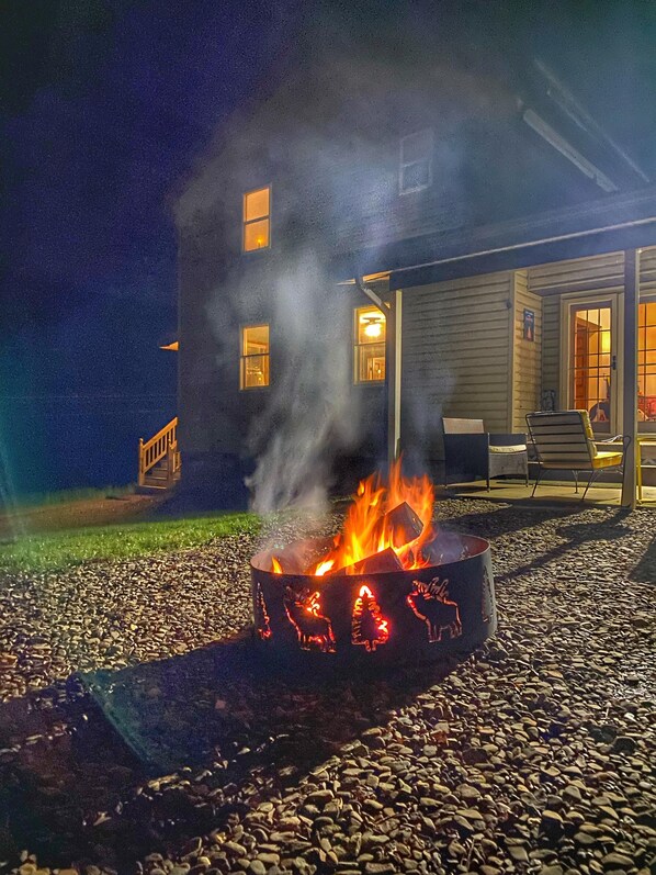 A fire pit with decorative animals, a building with multiple windows, and a patio area with outdoor furniture. - Large, 4 BR (1 King, 2 Queens), 2 Bath, Recently Renovated (Weedville)