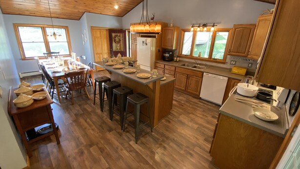 A spacious kitchen with wooden cabinets, a central island with stools, and a dining area with a table set for four. - Large, 4 BR (1 King, 2 Queens), 2 Bath, Recently Renovated (Weedville)