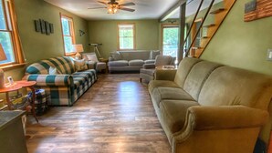 A spacious living room with hardwood flooring, a large sofa, a smaller couch, and a staircase. - Large, 4 BR (1 King, 2 Queens), 2 Bath, Recently Renovated (Weedville)