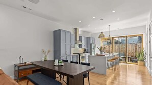Een moderne keuken met grijze kastjes, een centraal eiland met krukken, en een zithoek met een bank.