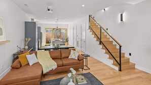 Een moderne woonkamer met een bruine bank, een eethoek en een trap.