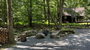 A forested area with a gravel path, large rocks, and a stack of firewood.