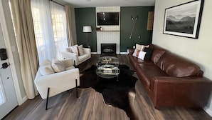 A living room with a fireplace, leather sofa, armchairs, and a coffee table.