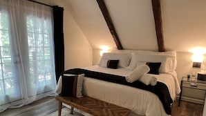 A bedroom with a large bed, a wooden bench, a nightstand, and a window with sheer curtains.