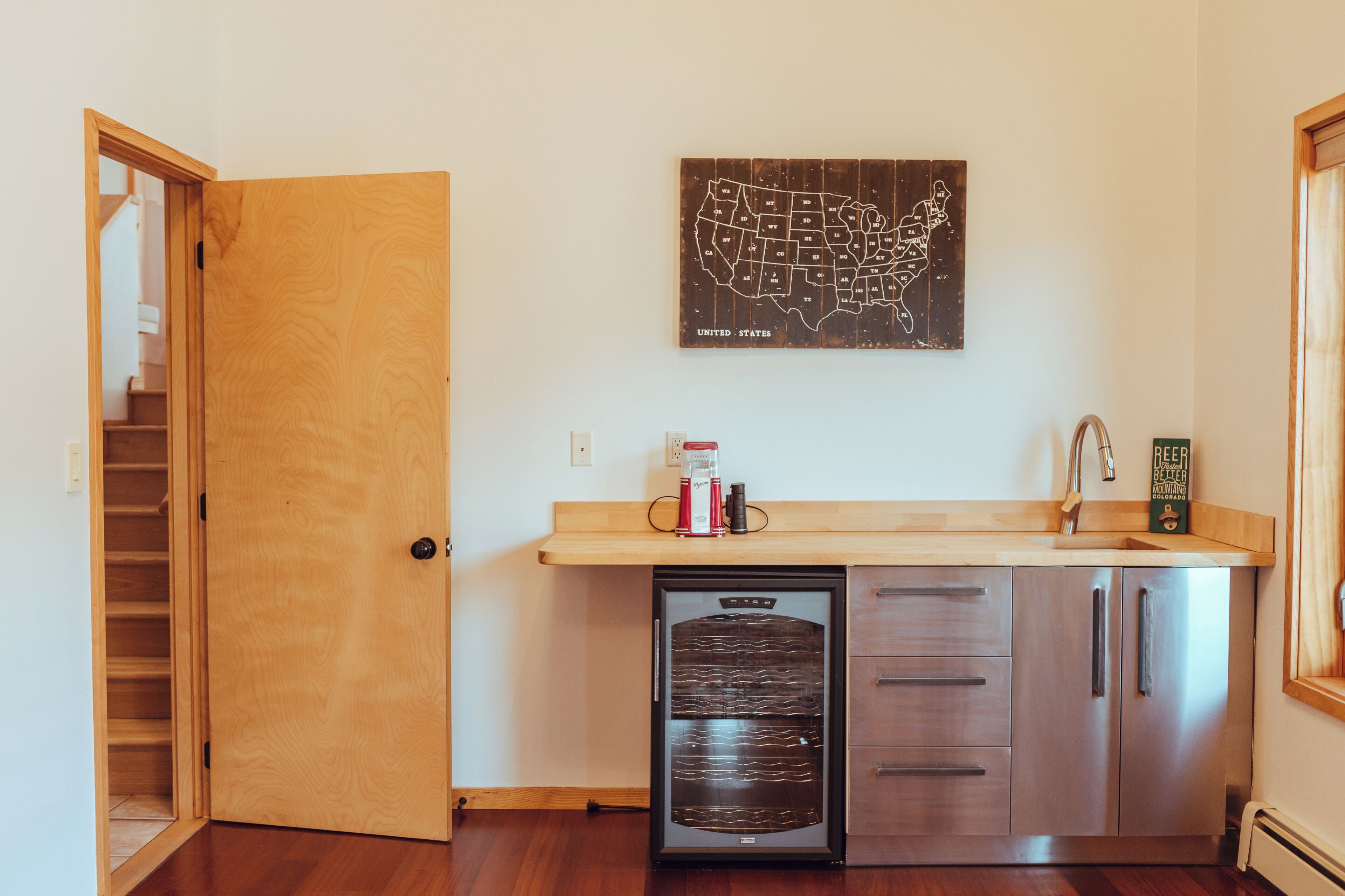 A compact kitchen with a wooden door, a refrigerator, a sink, and a wall-mounted map of the United States.