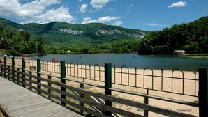 Une promenade en bois mène à une plage de sable, d’où l’on a une vue dégagée sur un lac et des montagnes en arrière-plan.