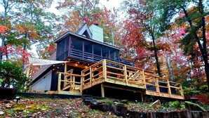 Une cabane en bois avec un étage supérieur en verre, entourée du feuillage automnal.