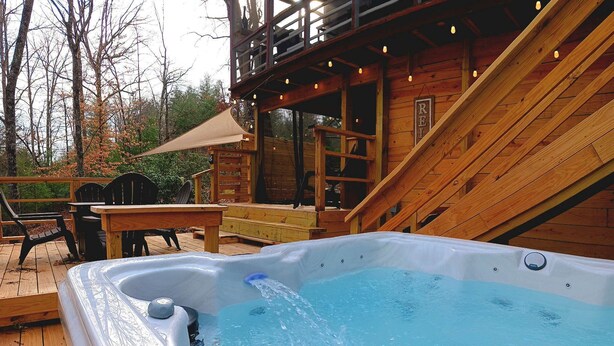 Un bain à remous sur une terrasse en bois, avec un escalier en bois et un espace salon couvert.