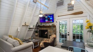 Un salon chaleureux avec une cheminée, un téléviseur fixé au mur et un coin repas comprenant une table et des chaises.