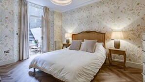 Un dormitorio con una cama grande, dos mesitas de noche con lámparas, papel tapiz con motivos florales y suelo de madera.