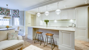 Una cocina moderna con armarios blancos, una isla central con taburetes, iluminación colgante y vistas al área de estar contigua.