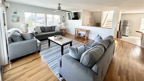 Uma sala de estar moderna com um sofá cinzento, uma mesa de centro e uma TV fixada na parede.