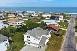 An aerial view of a coastal residential area with houses, a road, and the ocean in the background.