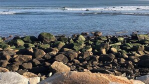 Uma linha costeira rochosa com grandes pedras e ondas ao fundo.