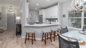A modern kitchen with white cabinets, a central island with stools, and a dining table with chairs.
