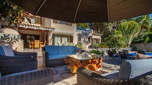 An outdoor patio area with wicker furniture, a glass-top coffee table, and a pool in the background. - El Salvador Fustera (Benissa)
